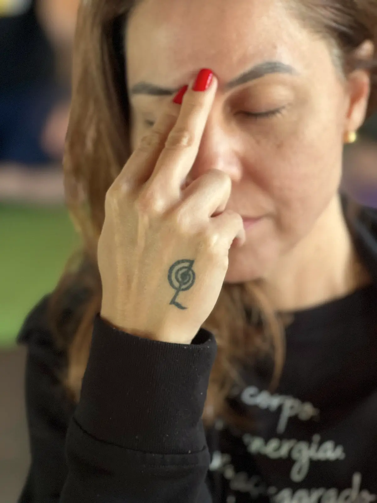 Luciane Lemos de olhos fechados tocando o ponto entre as sobrancelhas, com um símbolo do Reiki tatuado na mão