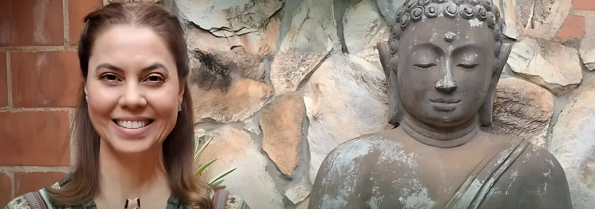 Luciane Lemos sorrindo com as mãos em namastê ao lado de uma estátua de Buda no Espaço Manipura