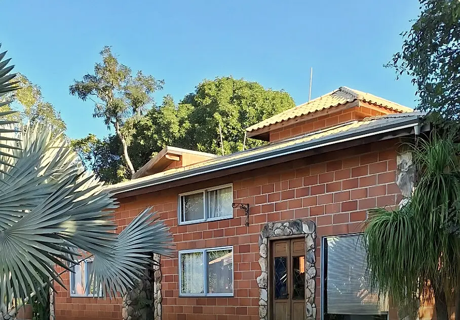 Casa de tijolos aparentes cercada por jardins e palmeiras