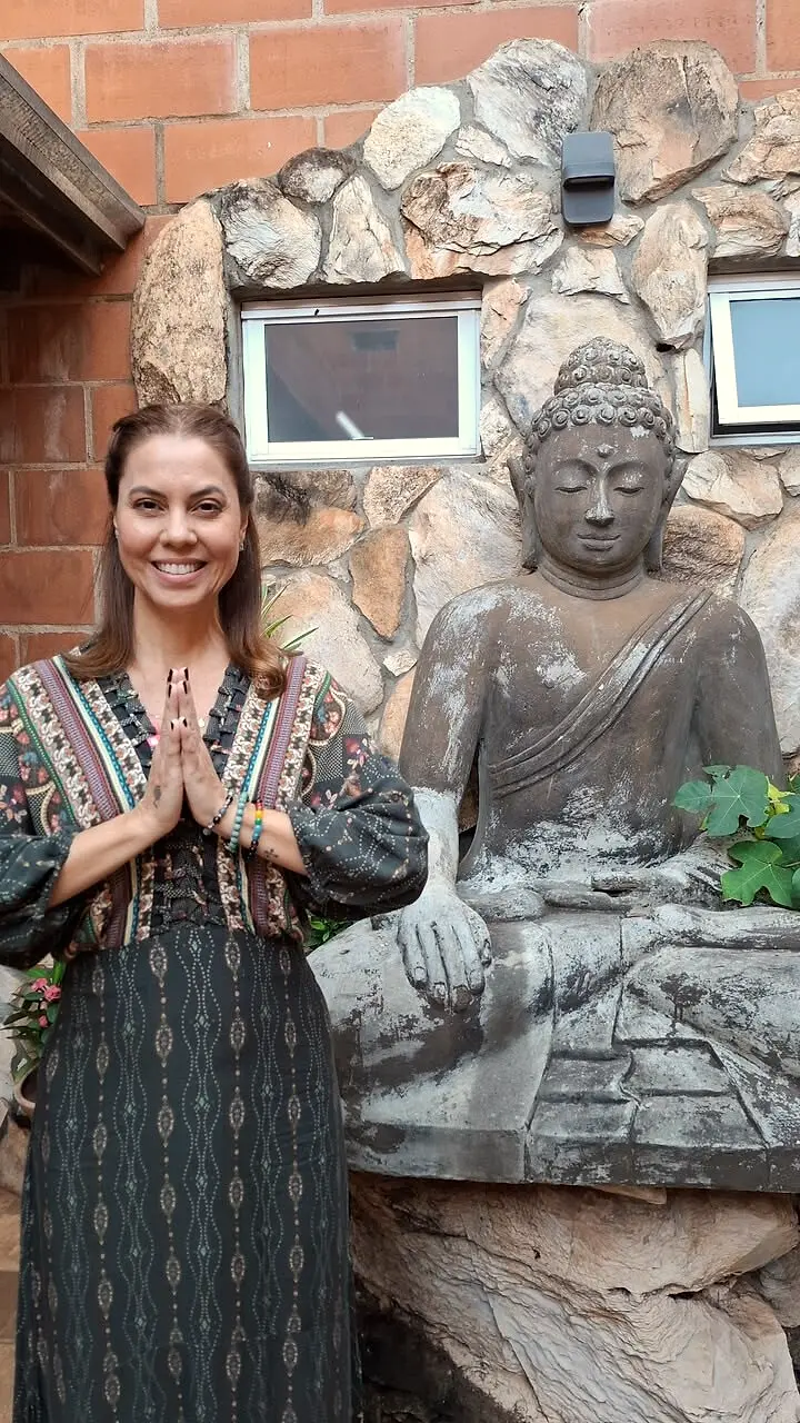 Luciane Lemos sorrindo com as mãos em namastê ao lado de uma estátua de Buda no Espaço Manipura