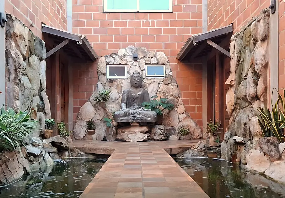 Caminho entre espelhos d’água levando a uma estátua de Buda em parede de pedras